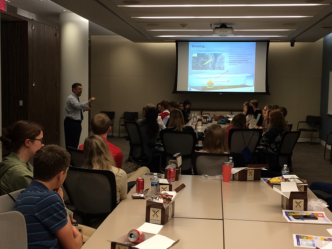 Students at two tables listening to Dr. Cohen present his slides