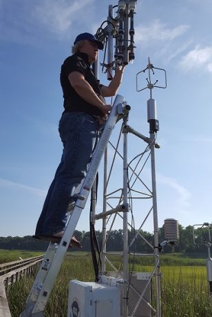 Man on a ladder installing equipment on a metal tower