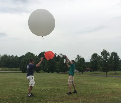 One man holding the bottom of the string as the other releases the large weather balloon