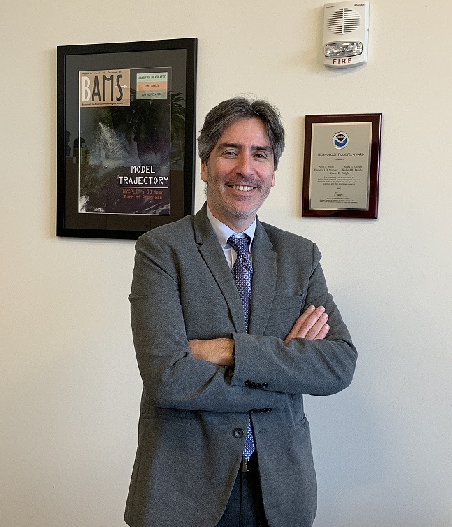 Dr. Stein standing in his office in front of a NOAA plaque and enlarged copy of an article that he authored