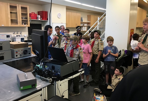 Kids, mostly in scout uniforms, crowded around Dr. Ren at a computer.