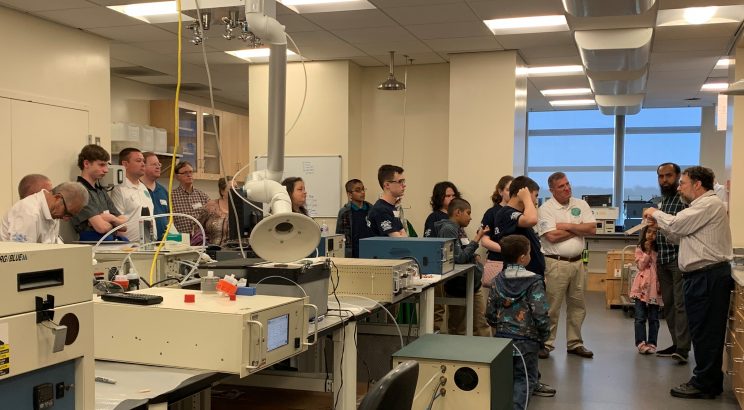 Scout troop, chaperones, and younger kids in the lab listening to Dr. Cohen