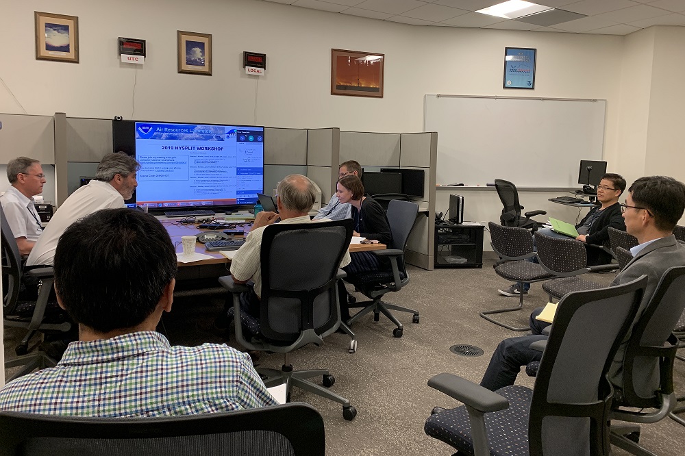 Eight people in front of a large monitor displaying a page showing 2019 HYSPLIT Workshop