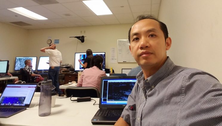 Close-up of Dr. Tang at his laptop sitting in a conference room.