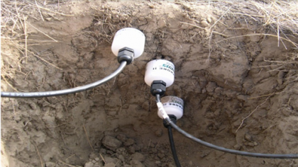 Three evenly spaced white cylinders with trailing cables in a hole in the ground