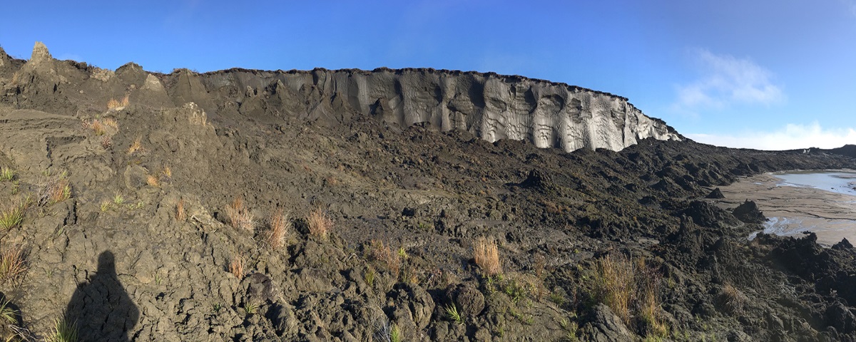 Rugged landscape with a hill descending to a river. The photographer's shadow is visible at the left.