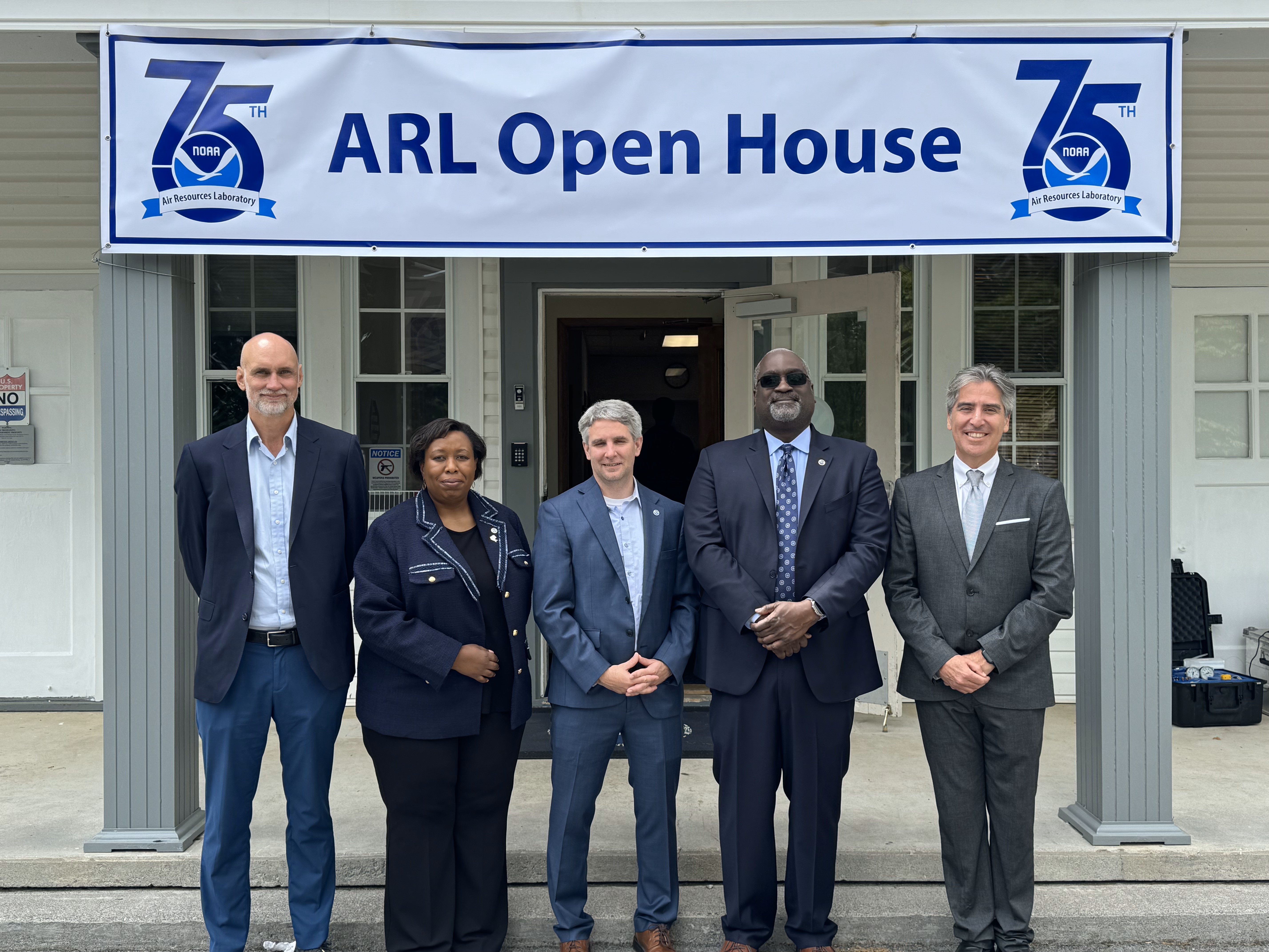 Five people in suits standing in front of a building with a banner above them that says ARL Open House