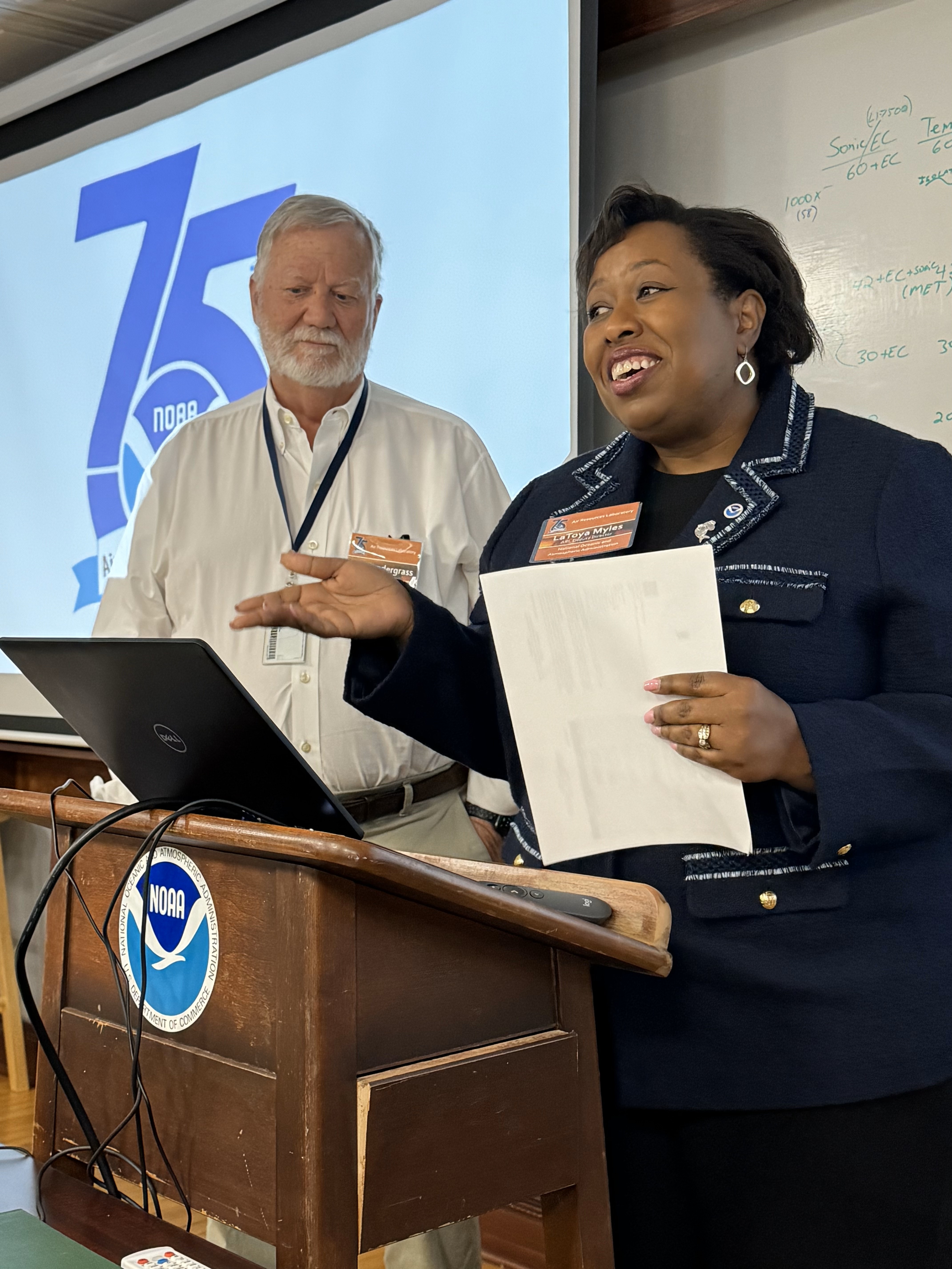 Woman talking at podium with an older man standing beside her