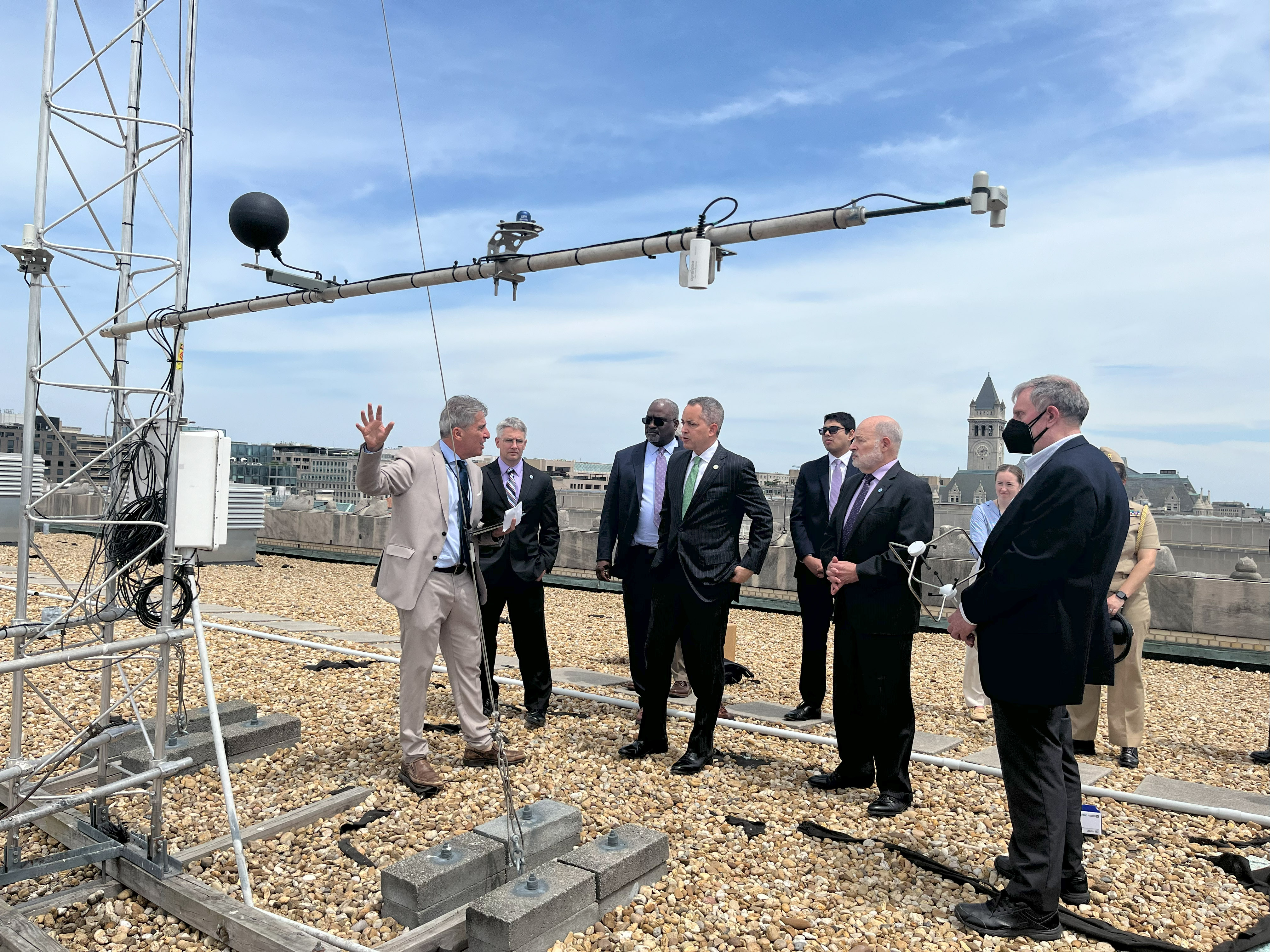 group of men in suits on a flat rooftop. metal scaffolding with scientific instruments in the foreground