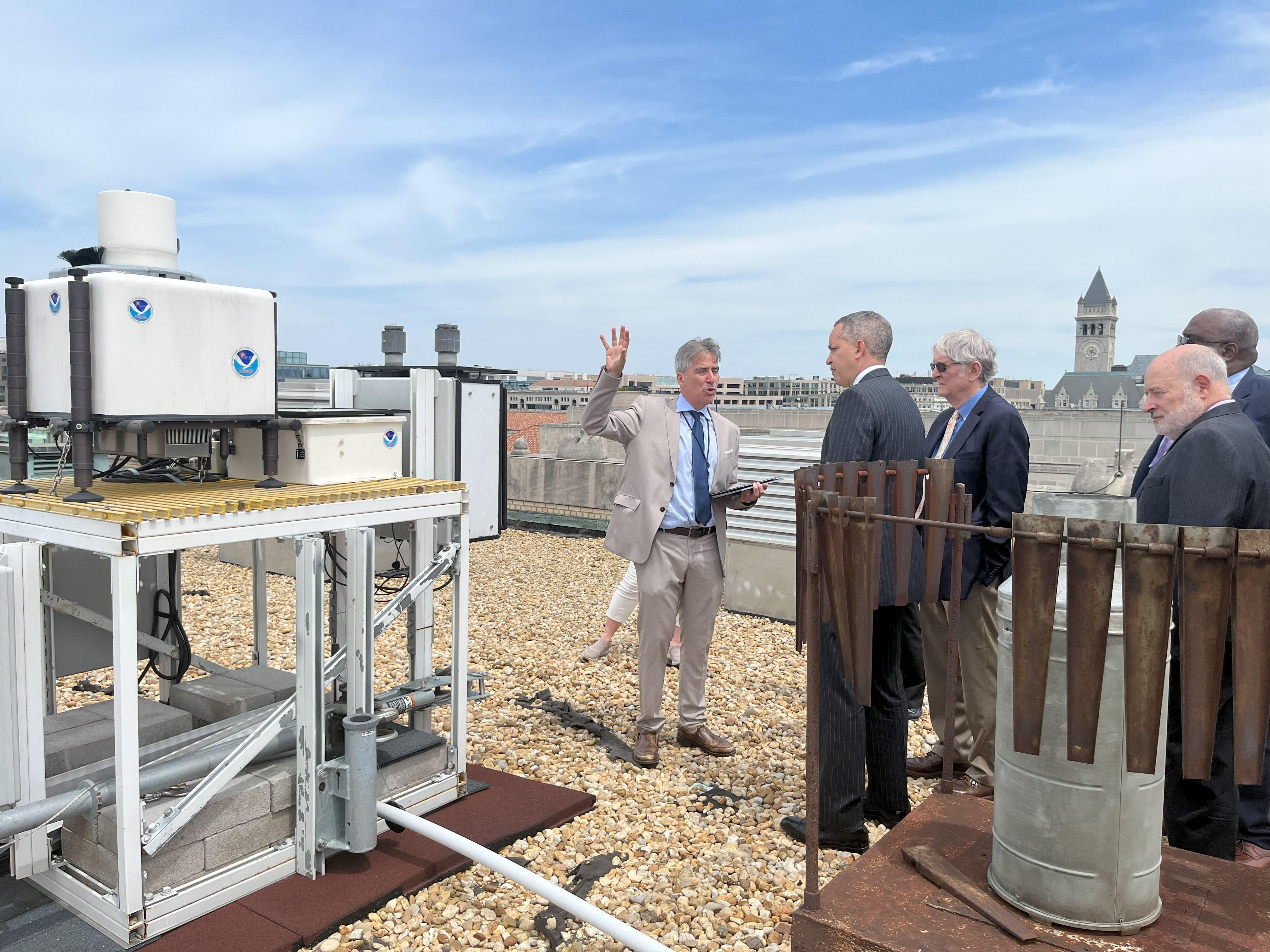 Group of men in suits gathered on a flat rooftop around scientific instrument box