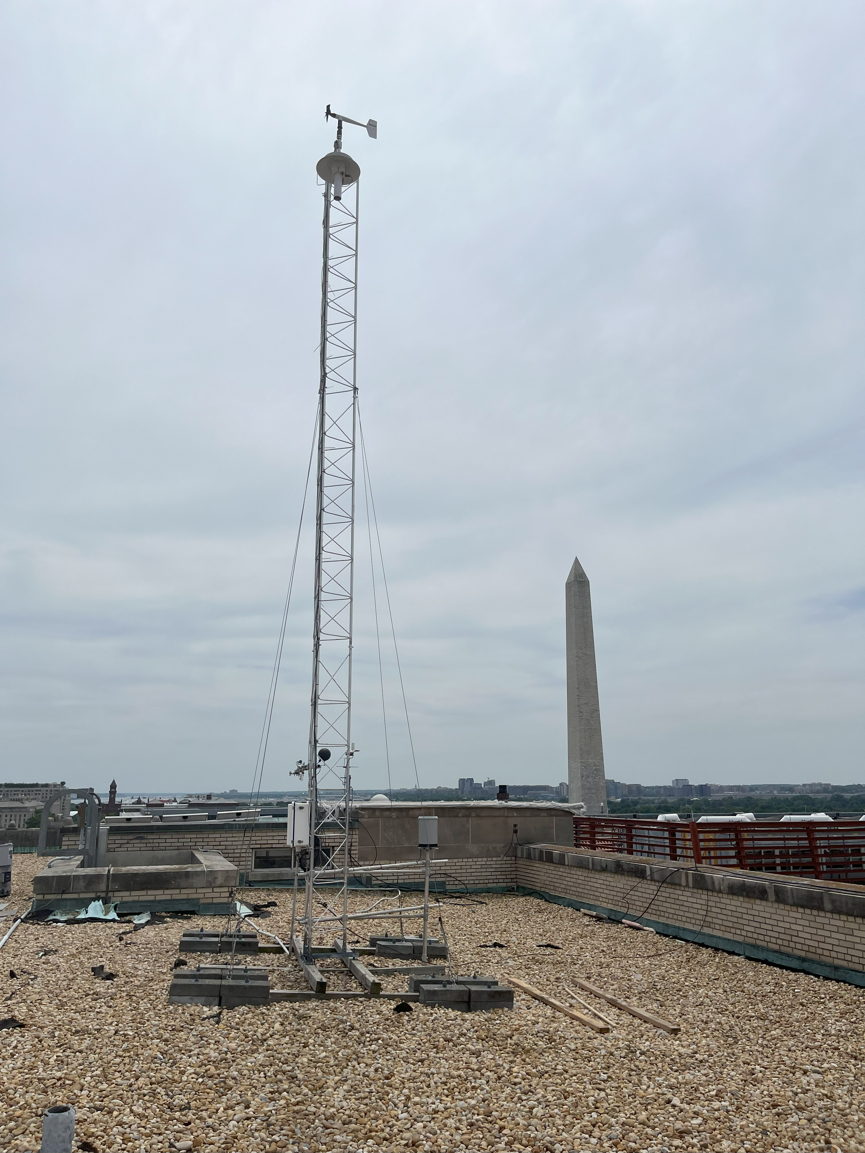Tower made of metal scaffolding mounted on a flat rooftop with the Washington Monument in the background.