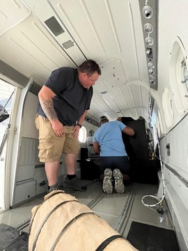 two men installing a rack in the empty cabin of an airplane