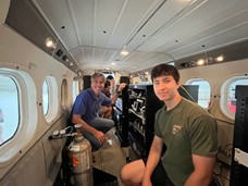 two men inside the cabin of a small plane with instrument racks inside.