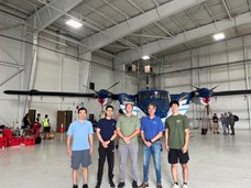 5 men standing inside an airplane hanger in front of a propeller plane