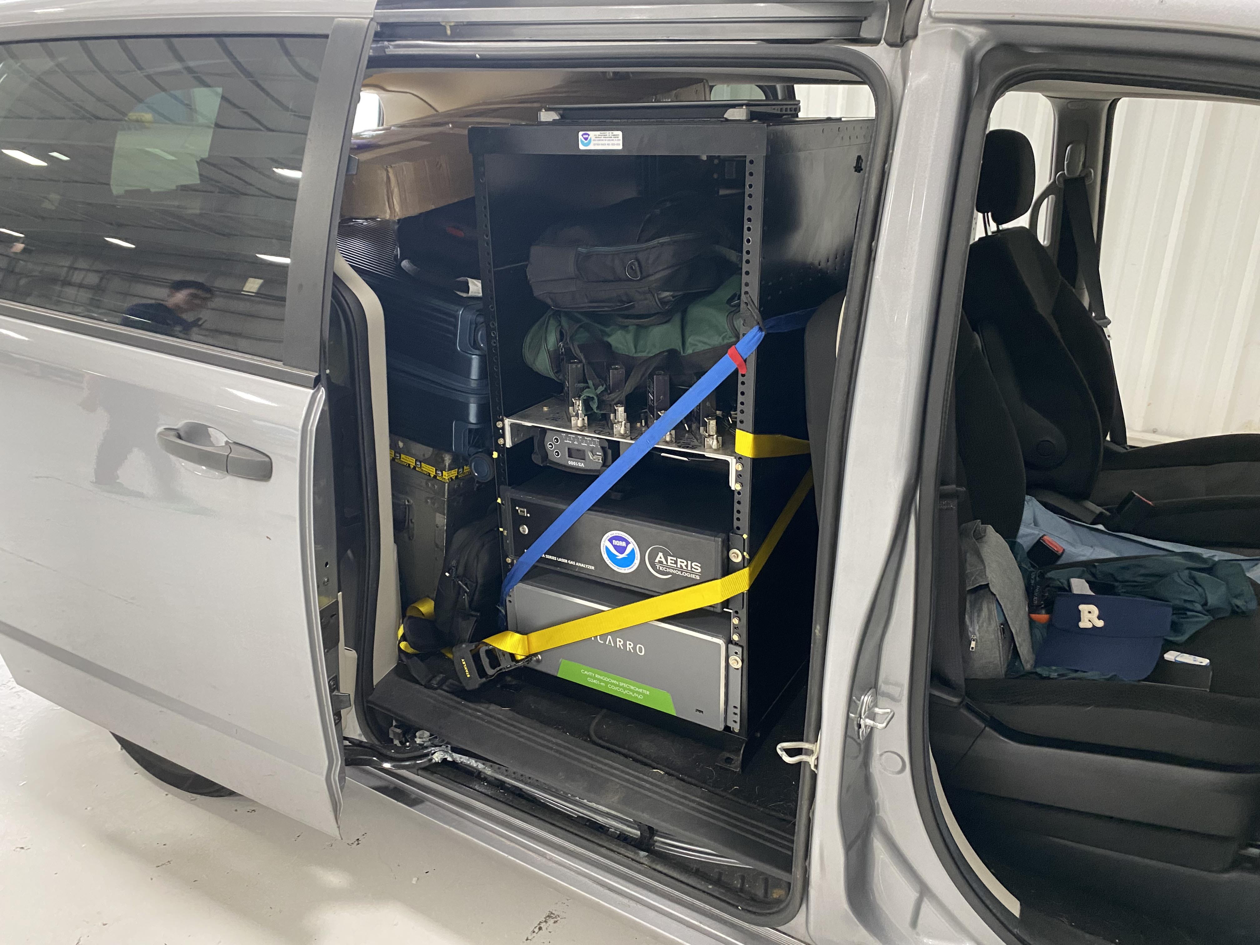Van with doors open so you can see suitcases, boxes, and a metal cabinet frame strapped down with NOAA electronics
