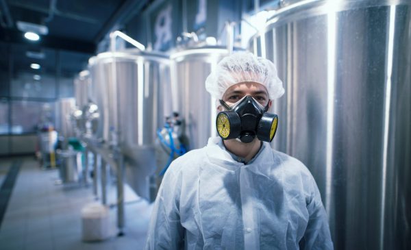 man in hazardous material gear standing in front of stainless steel tanks.